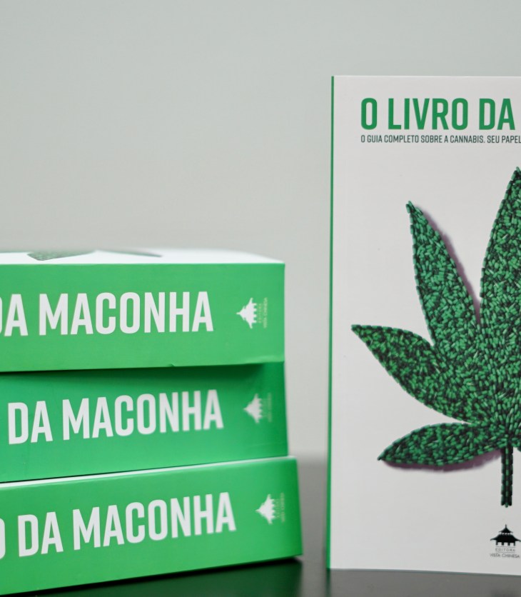 4 exemplares de O Livro da Maconha sobre uma mesa. Um de pé mostrando a capa e os outros 3 deitados com a lombada virada para frente.